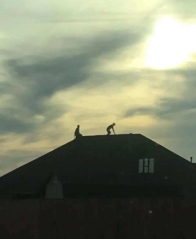 Two Diamond B roofers working on a hip roof against an Oklahoma sunset